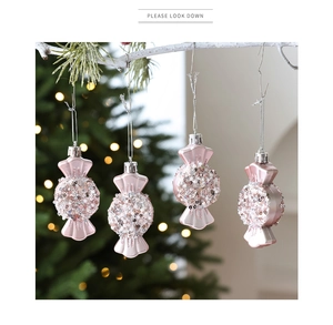 Detailed view of four pink candy-shaped Christmas ornaments with glitter hanging on branches