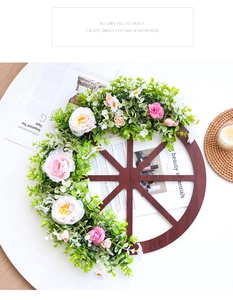 Rustic wooden wheel wreath detail with pink roses and green foliage on white surface