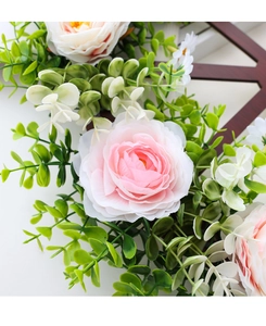 Close-up of pink silk roses and eucalyptus leaves on a dark brown wooden wheel frame