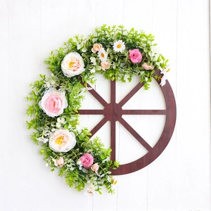 Rustic wooden wheel wreath with pink roses and green leaves on a white wood wall