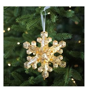 Detail of amber crystal snowflake ornament with white ribbon hanging on a Christmas tree