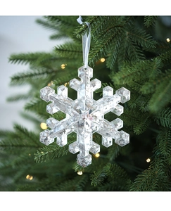 Macro detail of a transparent crystalline snowflake ornament on a glowing Christmas tree