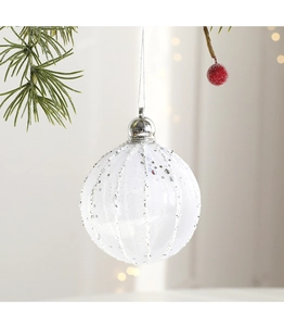 Dettaglio pallina di Natale bianca con strisce argento glitterate su pino verde