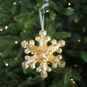 Sparkling amber crystal snowflake ornament with silver ribbon hanging on a Christmas tree