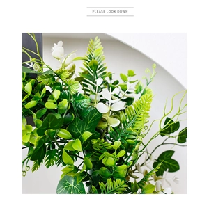 Close-up of realistic artificial wreath with green fern leaves and small white flowers