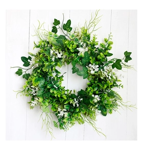 Detailed view of artificial green foliage wreath with small white flowers on white wood