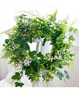 Close-up of lush artificial green leaf wreath with white flowers on white chair