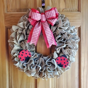 Detail of burlap Independence Day wreath featuring a red ribbon bow and ladybug accents