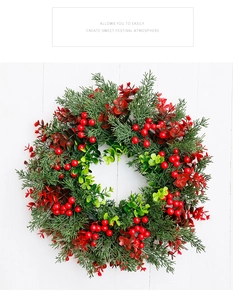 Detail van een kerstkrans met rode bessen en bladeren op een witte houten wand