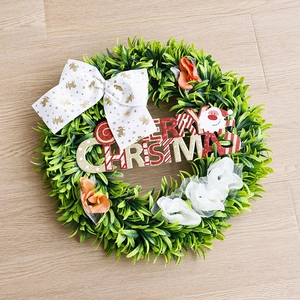 Artificial Christmas wreath with Merry Christmas sign, bow, and greenery on wood floor