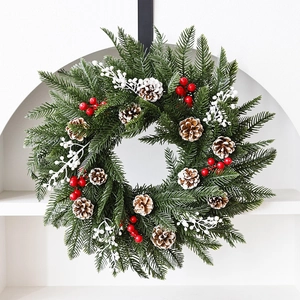 Couronne de Noël en PE avec pommes de pin et baies blanches sur un mur blanc pur