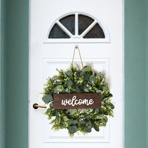 Artificial eucalyptus wreath with wooden welcome sign on white door for home decoration