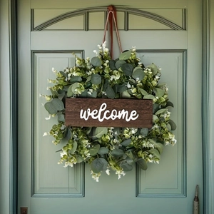 Close-up of artificial eucalyptus wreath with wooden welcome sign on a green door