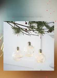 Hanging clear Christmas light bulbs with white sequins on pine branch with red berries