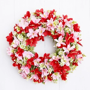 Spring wreath with red and pink artificial lilies and green leaves on white wood background