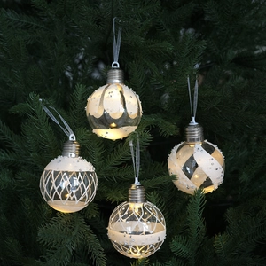 Set of four glowing clear Christmas balls with white glitter patterns on tree branches