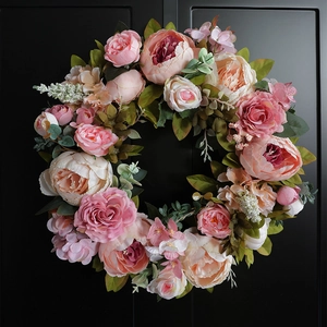 Detail of pink silk peony wreath with lush leaves hanging on a black textured door