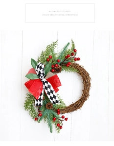 Detail of Christmas wreath with red berries, pine cones and checkered bow on white wood