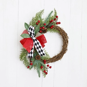Christmas wreath with green pine needles, red berries, and a plaid bow on a white wood base