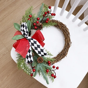 Christmas wreath with green pine branches, red berries and pinecones on a white wood chair