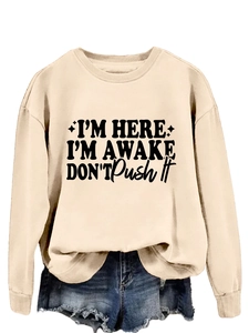 Detail of loose-fit beige sweatshirt featuring black text print and ribbed neck and cuffs
