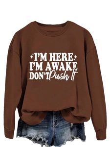 Close-up of brown sweatshirt with white I'M HERE I'M AWAKE text and denim shorts