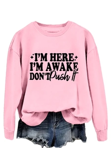 Detail of pink long-sleeve sweatshirt featuring bold black I'M HERE I'M AWAKE slogan print
