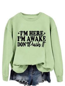 Detail of light green sweatshirt featuring 'I'M HERE I'M AWAKE' text and frayed denim shorts