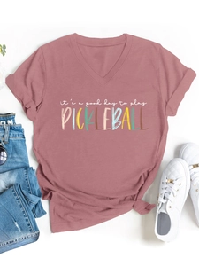 Dettaglio della t-shirt scollo a V rosa con slogan pickleball e accessori casual