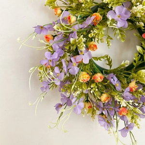 Detailed view of artificial purple garland with orange roses and green leaves