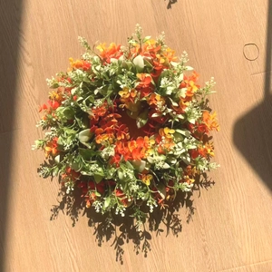 Detailed view of artificial eucalyptus wreath with orange flowers on light wood background