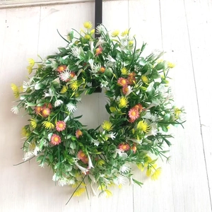 Detail of colorful artificial wildflower wreath with green leaves on white wood