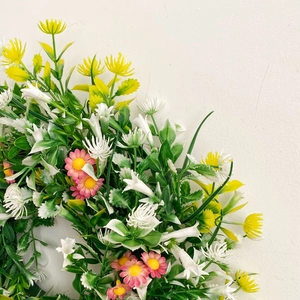 Close-up of spring wreath featuring white lilies, yellow daisies, and lush green leaves