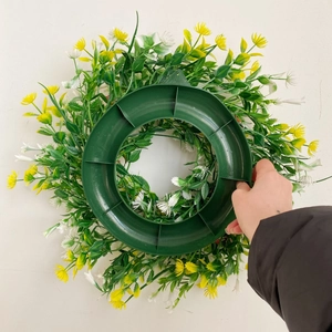 Artificial spring wreath with yellow and white flowers on a green plastic circular frame