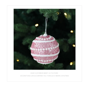 Detail of pink glitter Christmas ball with white pearl accents hanging on a festive tree