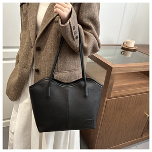Detail of black pebbled leather tote bag showing vertical stitching and fashion label