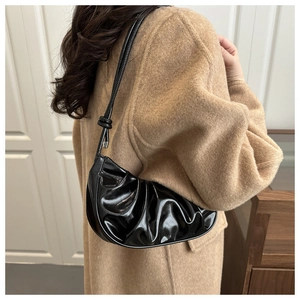 Detail of black glossy patent leather crescent bag with pleated texture on wool coat
