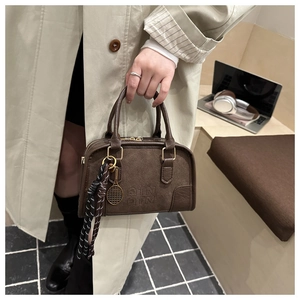 Dettaglio della borsa Boston marrone con logo QTN in rilievo e ciondolo da tennis dorato