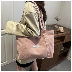 Macro view of a large pink corduroy tote bag showing side shoulder wear and fashion label