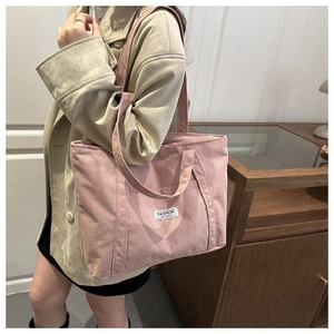 Detail of pink corduroy tote bag with fashion label shown on beige trench coat