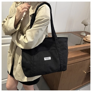 Detail view of black corduroy tote bag worn on shoulder featuring a fashion instinct label