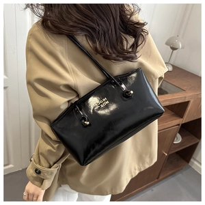 Close-up of black glossy patent leather tote with gold metal lettering on shoulder strap