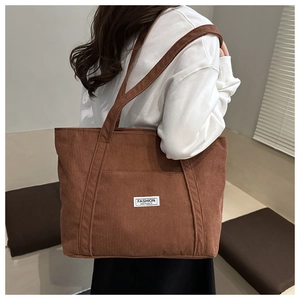 Rear view of a model wearing a brown corduroy tote bag with white fashion label