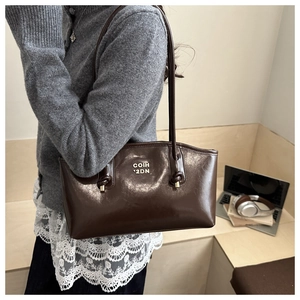 Detail of dark brown leather shoulder bag with metallic logo and knot strap accents