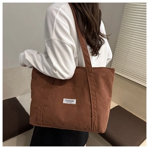 Macro detail of brown corduroy tote bag showing vertical ribs and fashion label patch