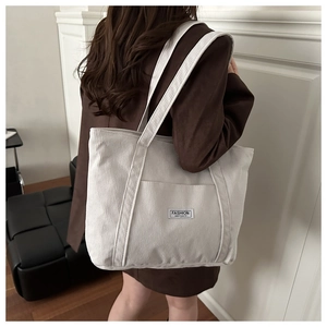 Detail of off-white corduroy tote bag with Fashion Instinct label worn by a model