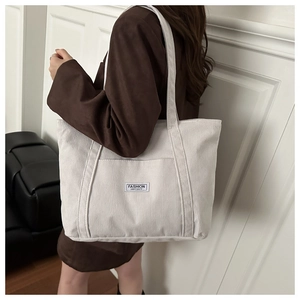 Close-up of white corduroy tote bag featuring a fashion logo patch and shoulder strap