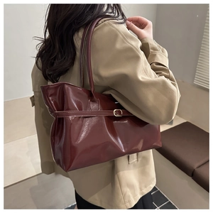 Close-up of a burgundy oil wax leather tote bag worn on shoulder by a model