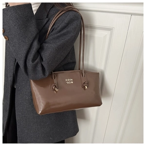 Detail of a brown leather shoulder bag with fine knot strap and metallic logo lettering