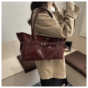 Detail of burgundy patent leather tote bag with glossy finish and gold metal buckle